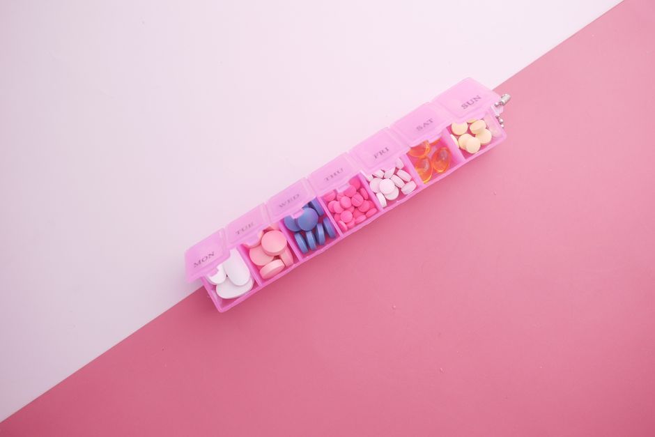 A pink pill organizer with colorful tablets arranged for each day of the week on a vibrant pink background.