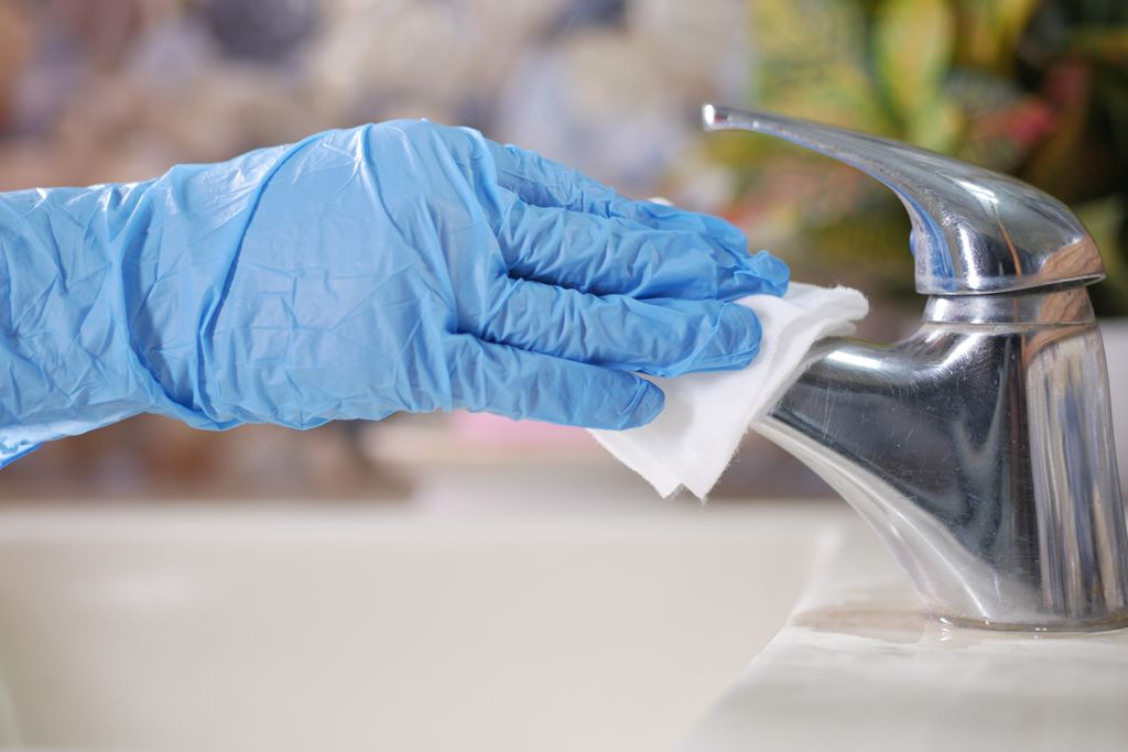 Hand in blauwe handschoen wrijft een verchroomde kraan droog met een doek