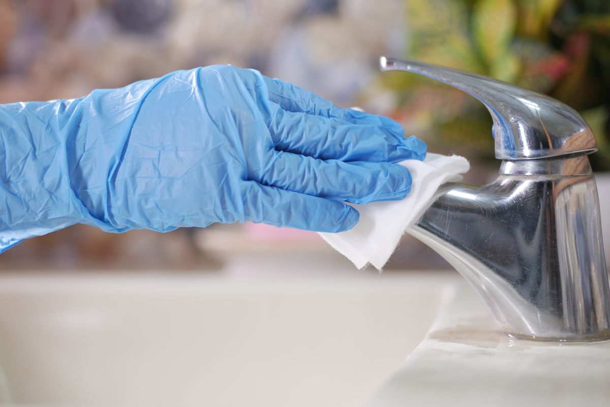Blue-gloved hand wiping a chrome faucet with a white cloth