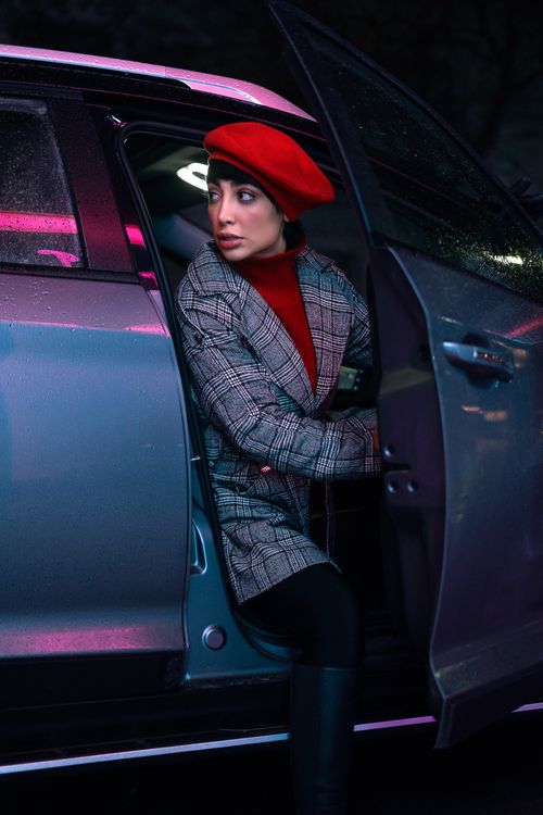 Free Stylish woman in red beret exiting a car at night under neon lights. Stock Photo