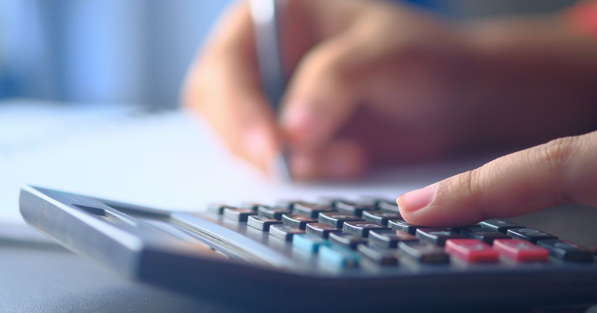 Close-up of hands working on a calculator and writing notes