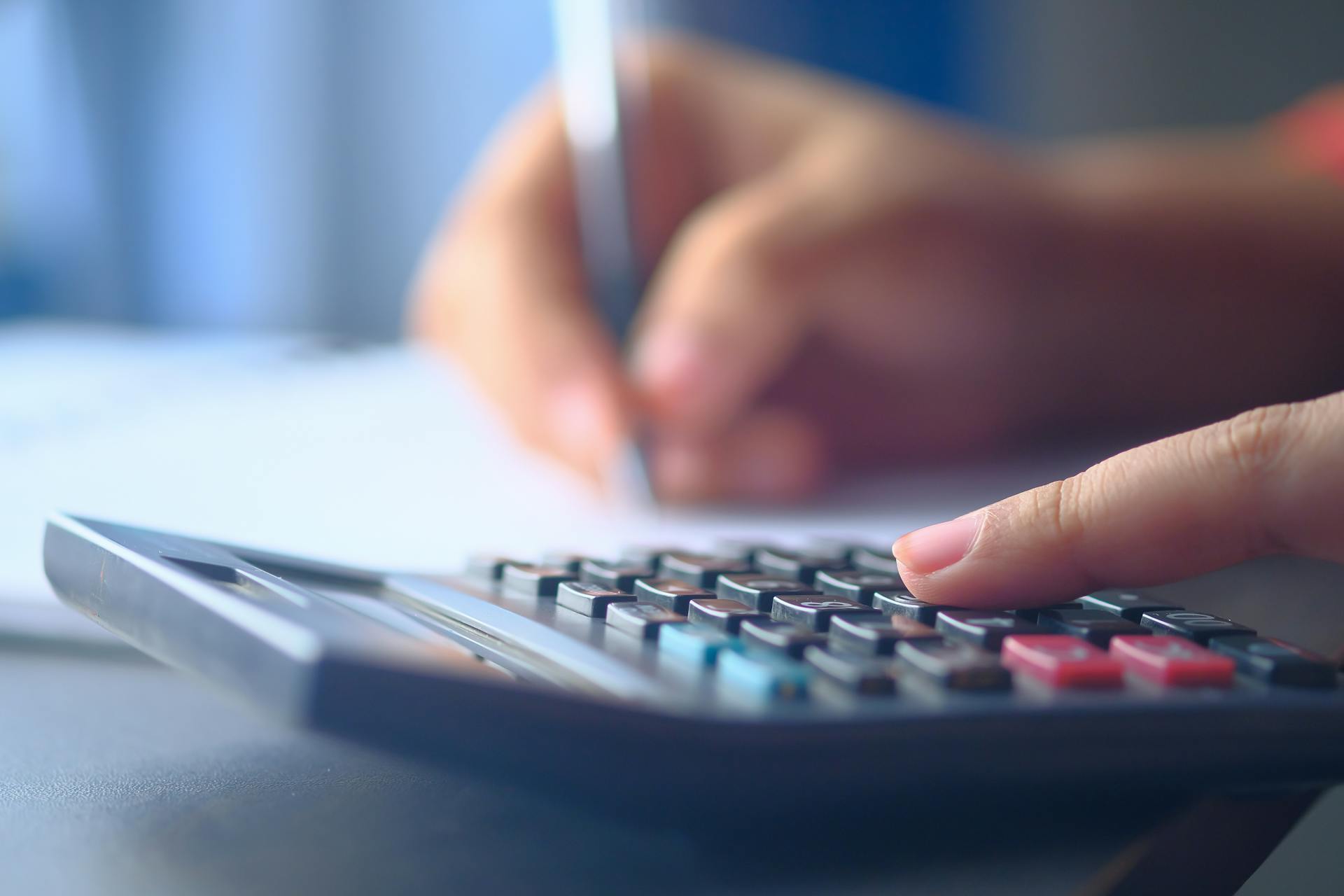 A close-up image of hands working on a calculator and writing, representing budgeting and financial planning.