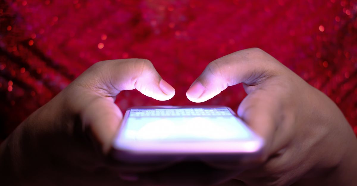 A person's hands using a smartphone with a glowing screen in low light