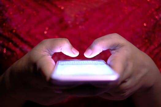 Hands typing on a smartphone with a glowing screen in low-light, highlighting technology and communication.
