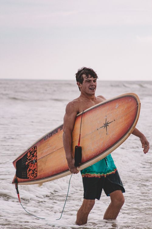 Free Energetic young man carrying a surfboard on New Smyrna Beach in Florida. Stock Photo