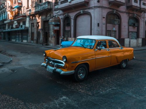 Free Classic yellow Ford car driving through an urban street, showcasing vintage style and charm. Stock Photo