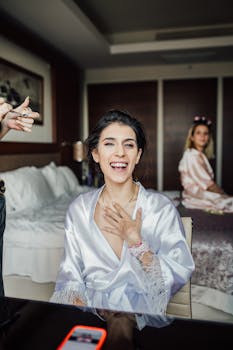 A joyful woman in a satin robe is laughing in a bridal suite, exuding happiness and elegance.