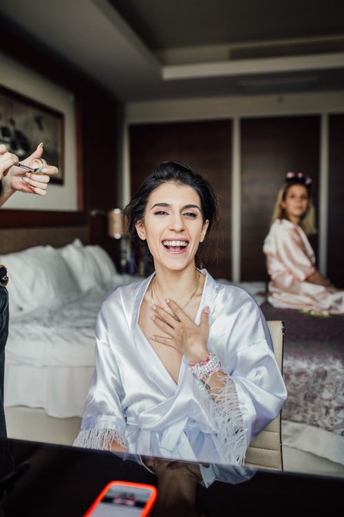 Free A joyful woman in a satin robe is laughing in a bridal suite, exuding happiness and elegance. Stock Photo