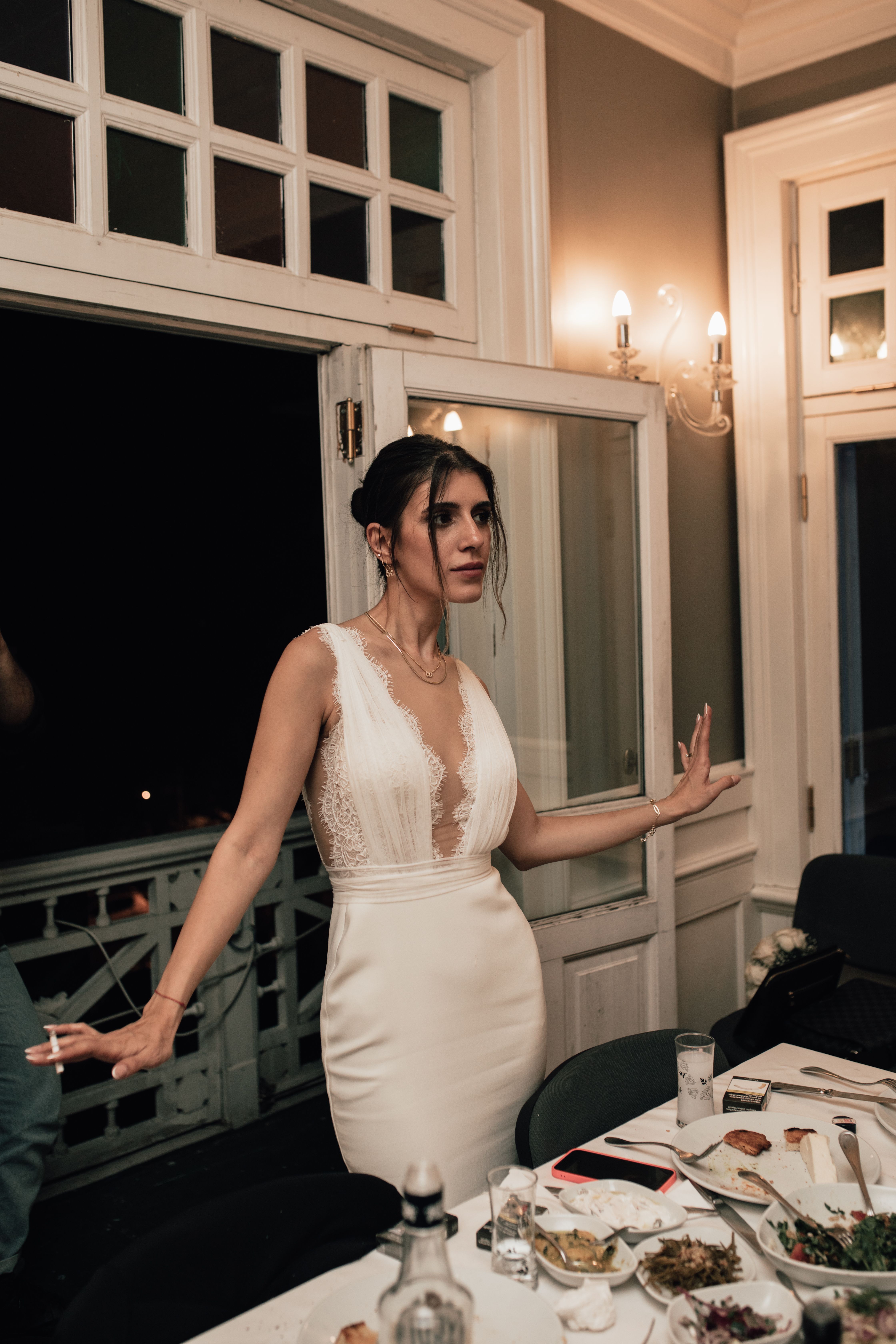Bride in elegant white dress near balcony during evening indoor reception.