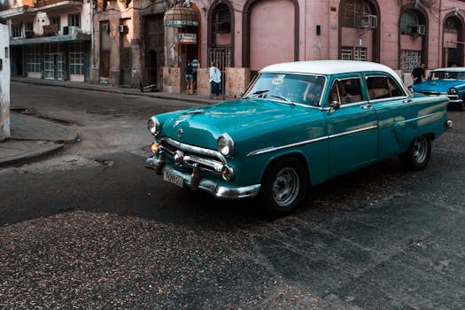 Classic blue car driving on a historic city street with buildings in the background.