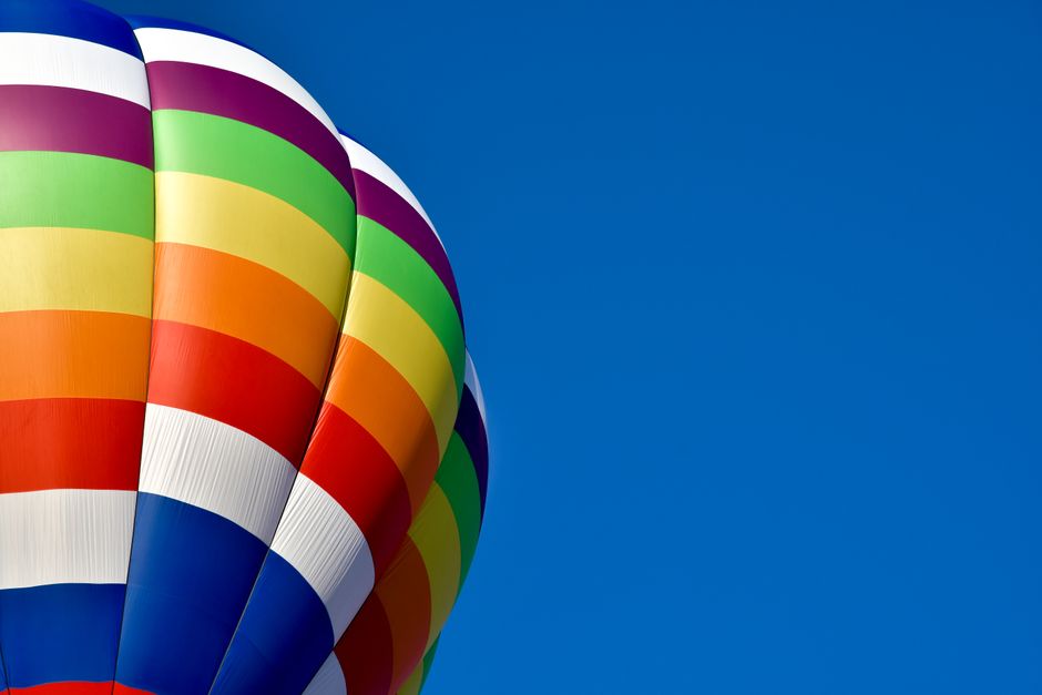 A colorful hot-air balloon catches the eye with its vivid stripes against a clear blue sky, embodying a sense of adventure.