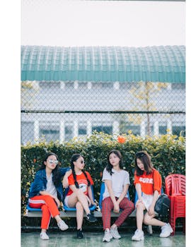 Stylish teen girls sitting outdoors in casual fashionwear, enjoying leisure time together.