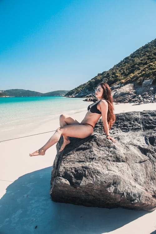 Free Beautiful Woman in Bikini Sitting on the Rock on the Beach  Stock Photo