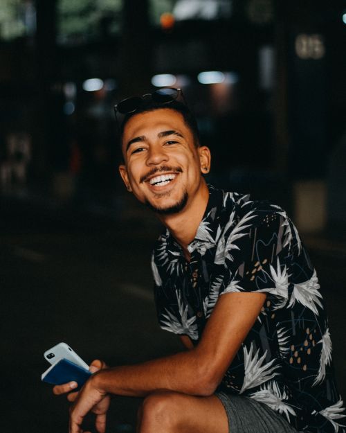 Free Portrait of a young man smiling with a smartphone in hand, on a dimly lit city street at night. Stock Photo
