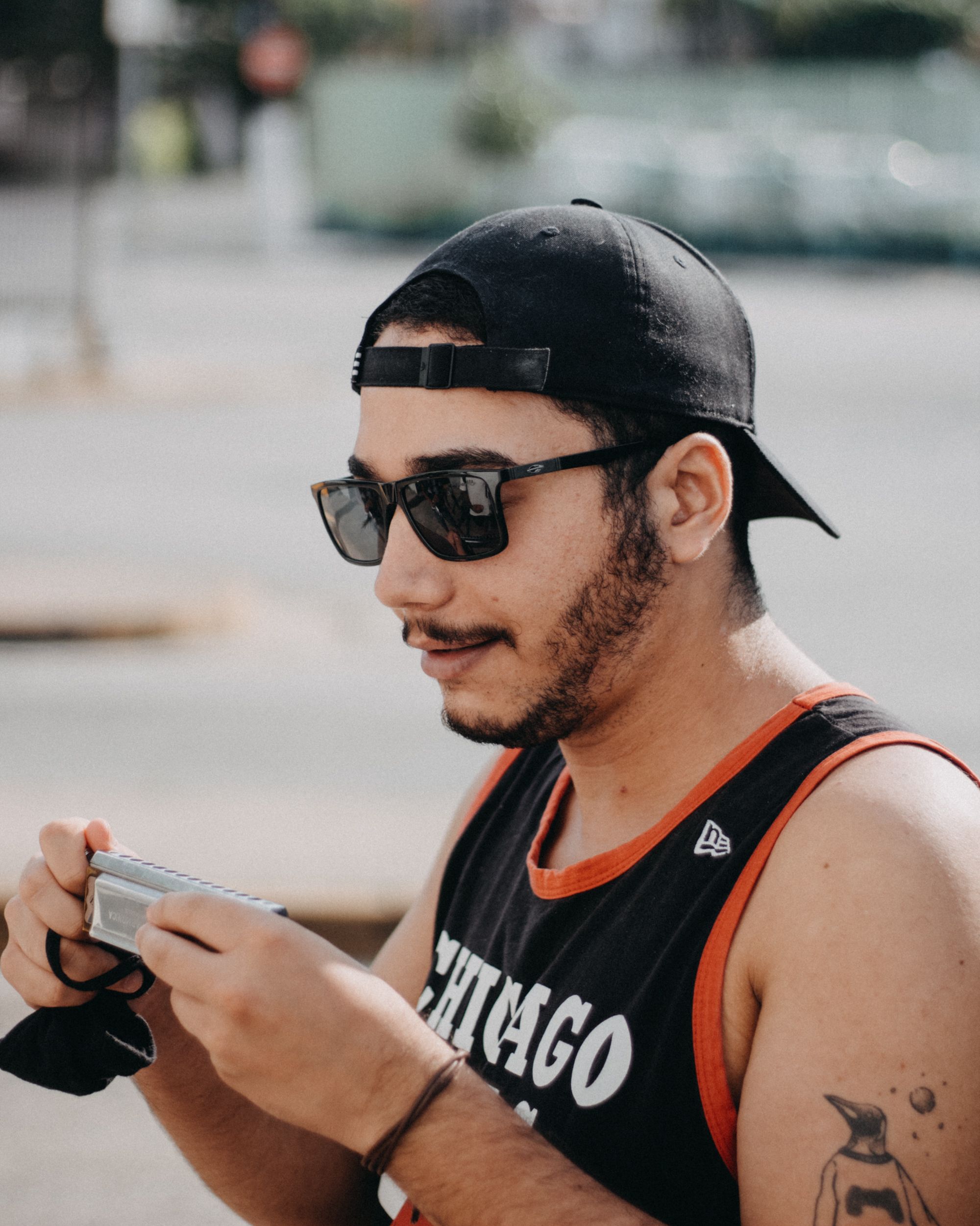 A young man wearing sunglasses and a cap, holding a camera outdoors.