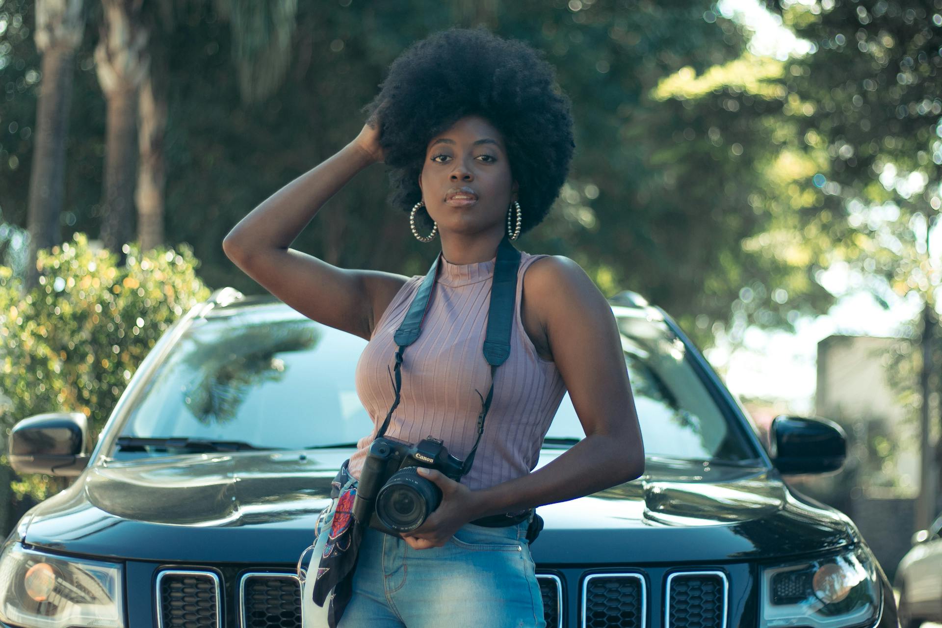 African woman posing with a DSLR camera and car outdoors.