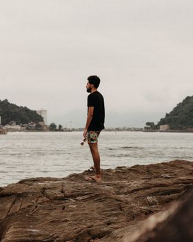 A man stands on a rocky shore, gazing into a lake under a gloomy sky, embodying tranquility and solitude.