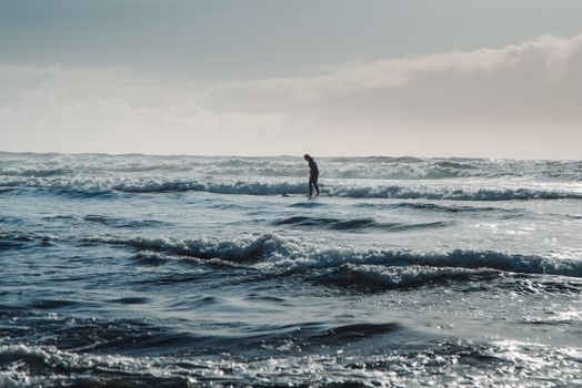 A surfer skillfully rides waves under a clear blue sky on Oregon's scenic coastline.