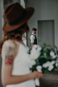 Creative indoor wedding portrait with bride holding bouquet and groom in background.