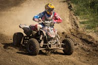 白天，一名戴着头盔的骑手驾驶四轮摩托车，在泥泞的小路上飞驰，尽显刺激与冒险