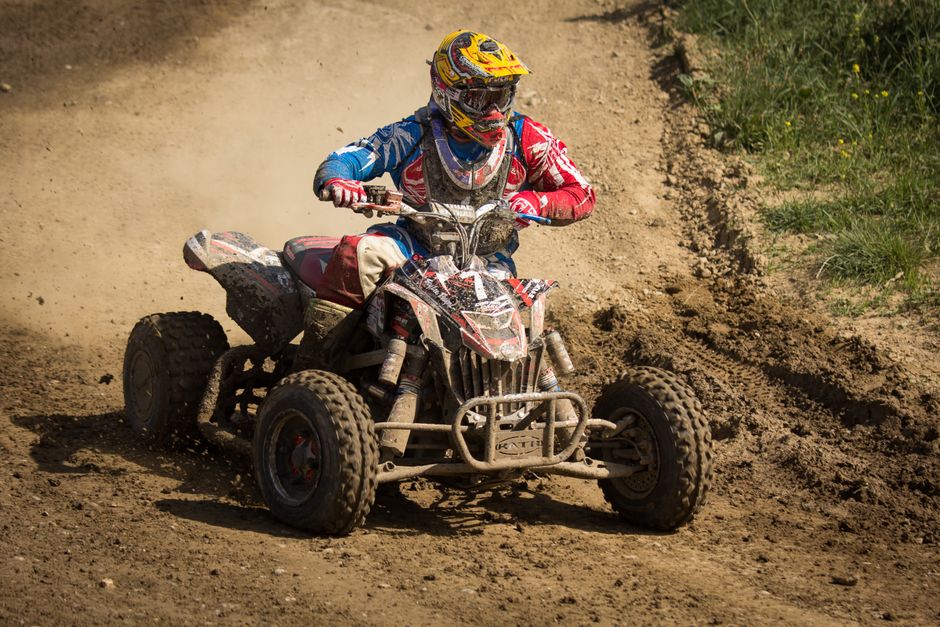 Helmeted rider on a quad bike speeding through a dirt track during daytime, showcasing thrill and adventure.