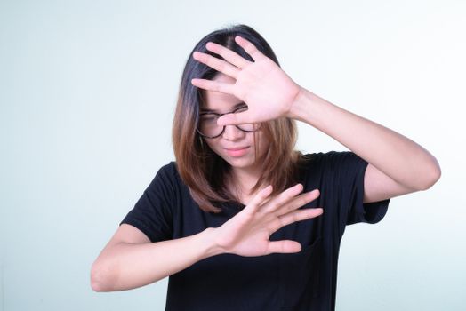 A young Asian woman with glasses playfully covers her face with her hands in a casual pose.