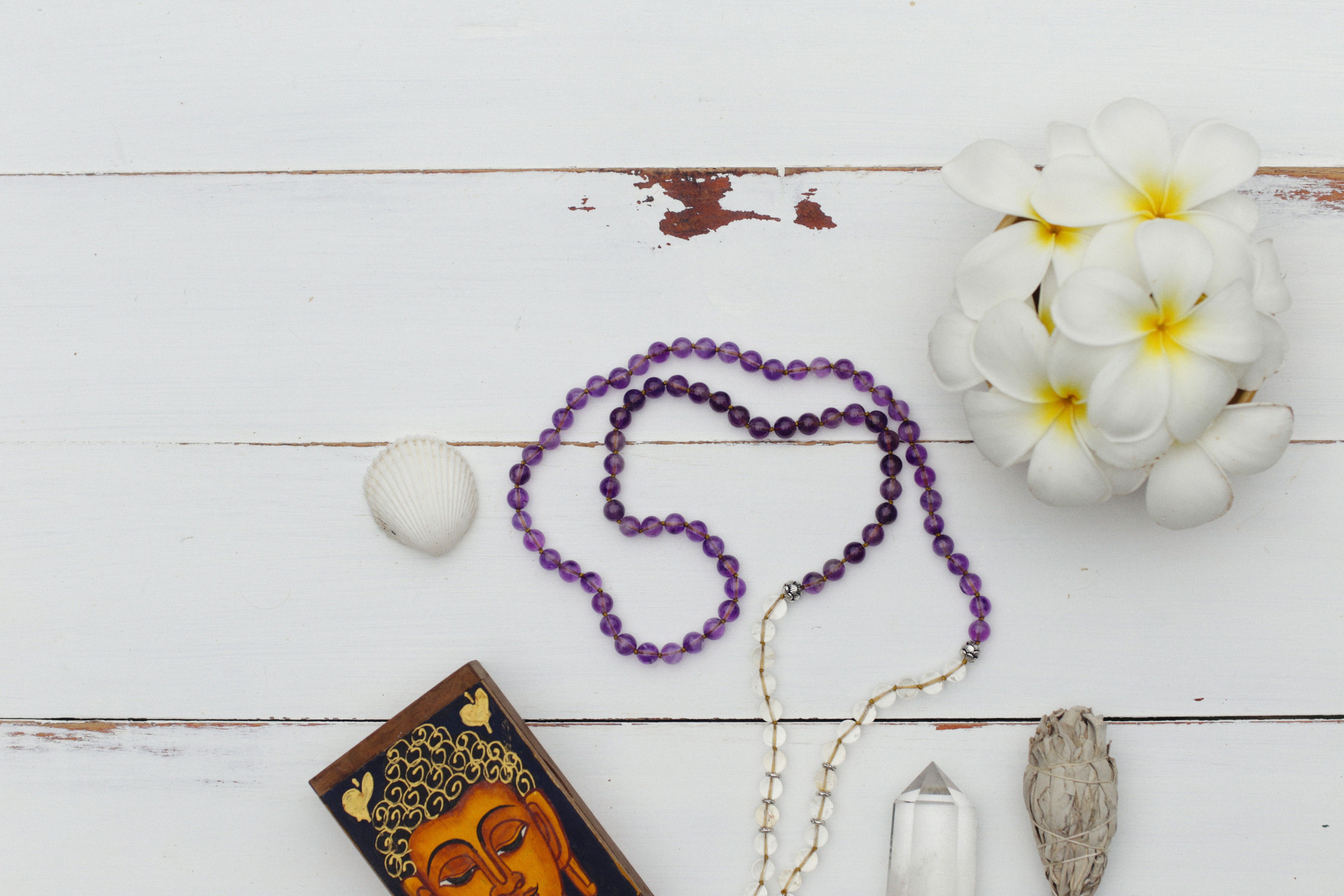 A stylish flat lay composition featuring beads, flowers, and spiritual elements against a white wooden background.