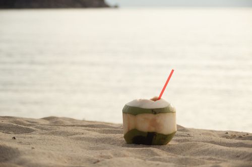 Free A coconut drink with a straw sits on a sandy beach, perfect for a summer refreshment. Stock Photo