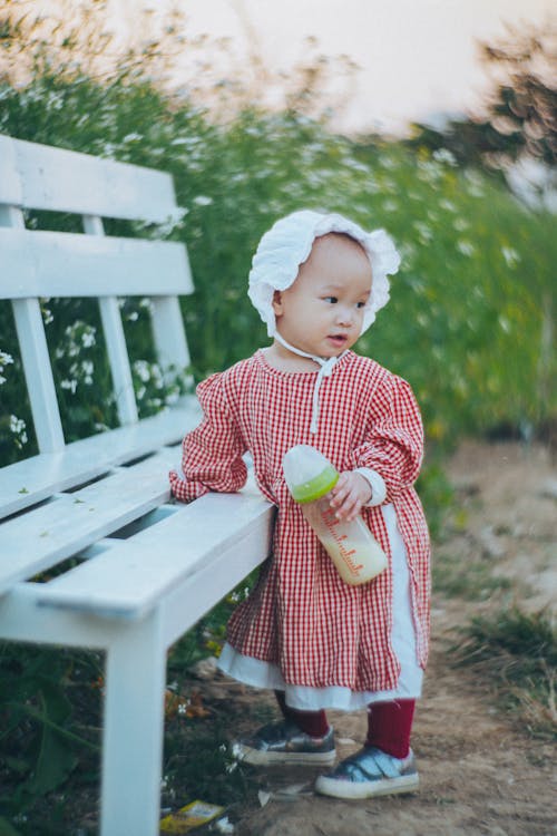Toddler in Red Plaid Dress leaning in a Wooden Bench 