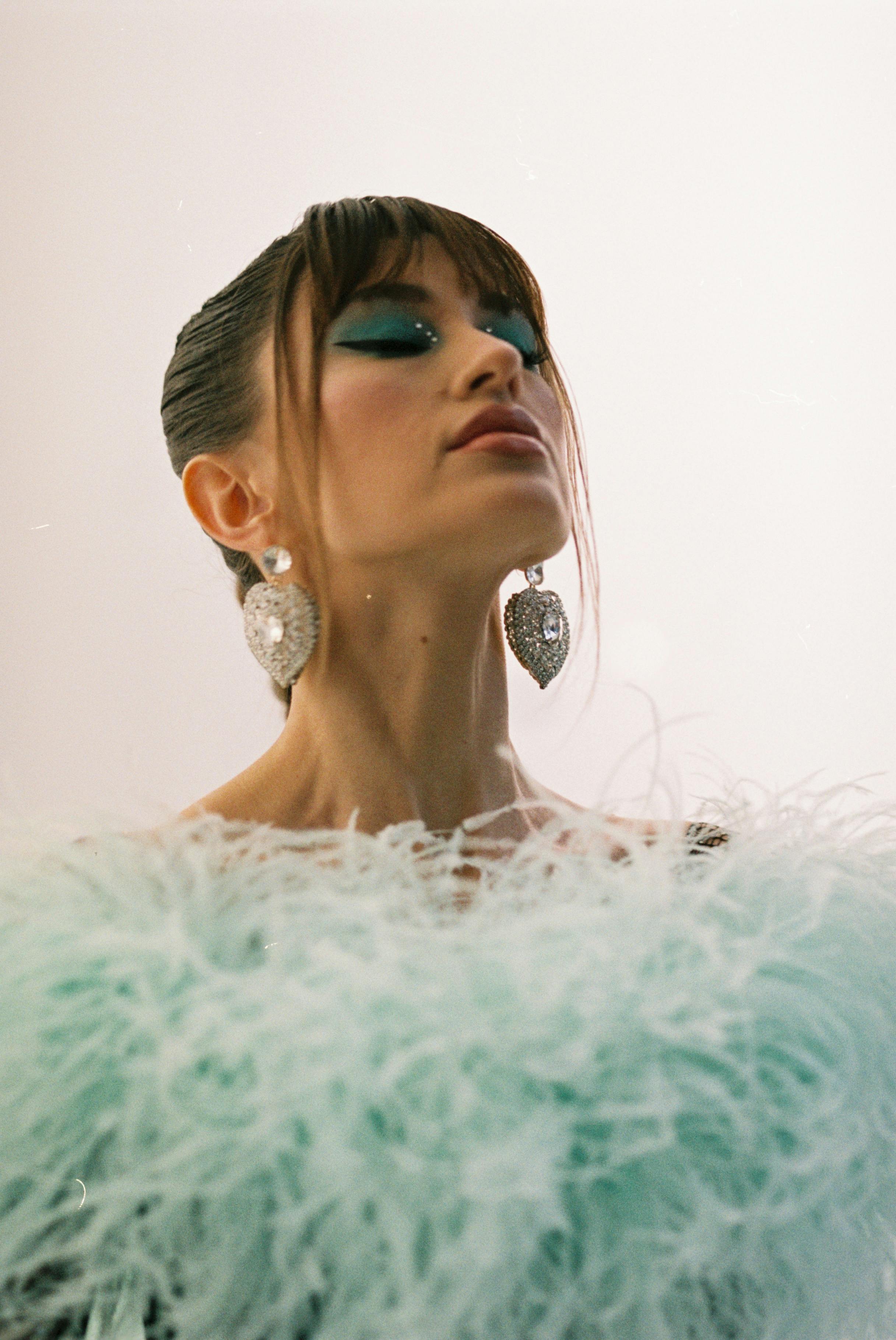 Portrait of a stylish woman with striking blue makeup and statement earrings, conveying confidence and elegance.