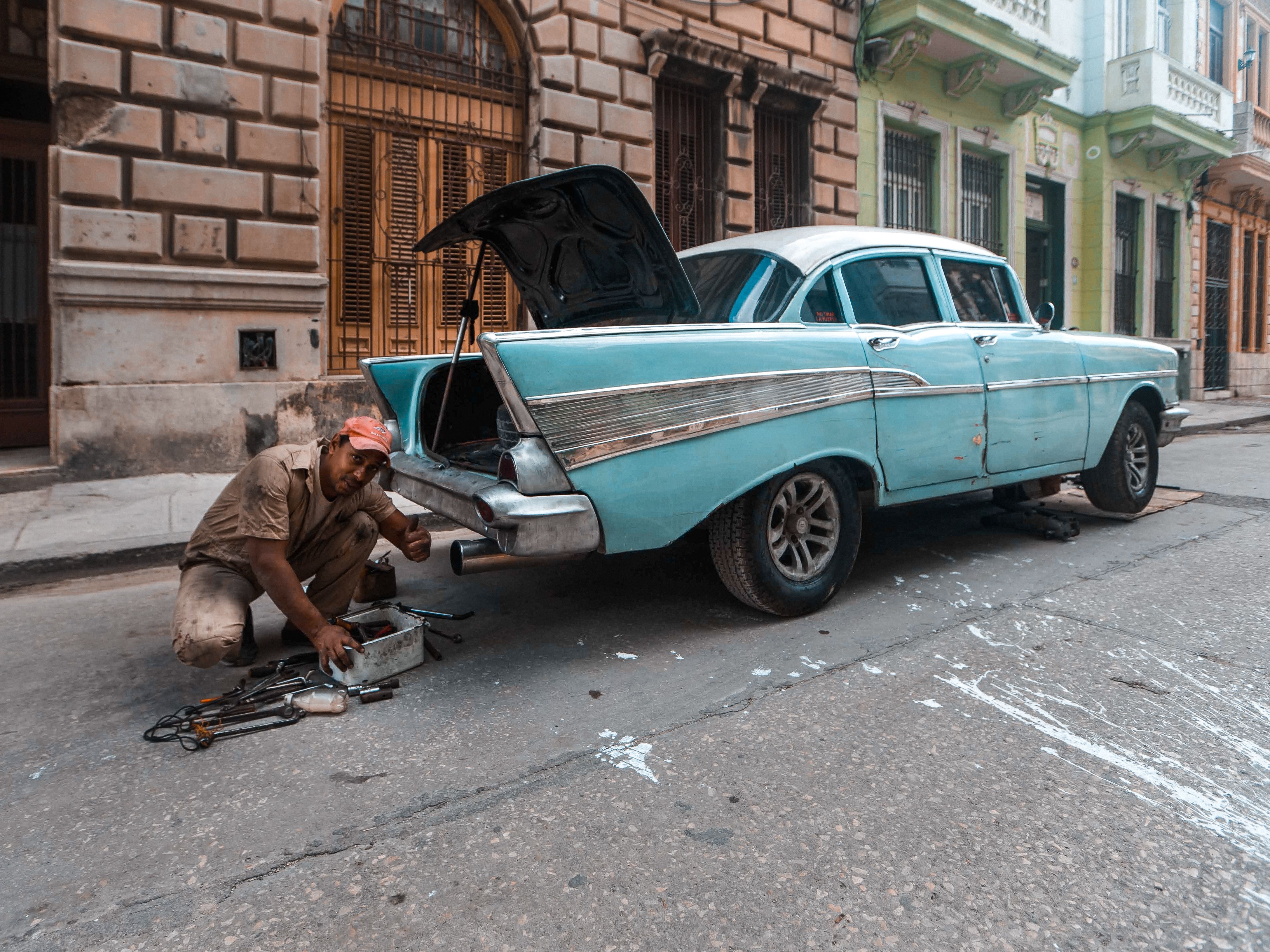 A mechanic repairs a vintage car on a historic city street, showcasing classic auto maintenance.