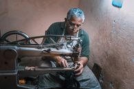 Elderly artisan meticulously operates a vintage sewing machine in a rustic workshop setting.