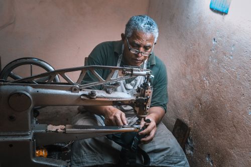 Free Elderly artisan meticulously operates a vintage sewing machine in a rustic workshop setting. Stock Photo