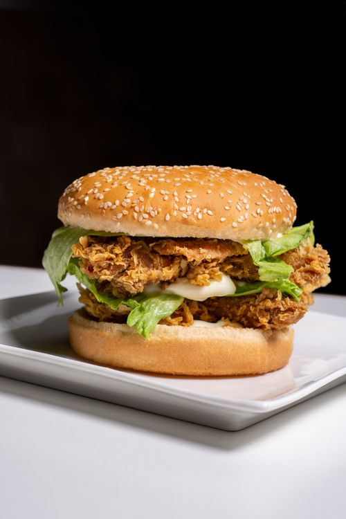 Free Close-up of a crispy fried chicken burger with lettuce on a white plate. Stock Photo