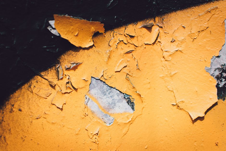 Close-up of peeling, blistered yellow paint on a damp-damaged exterior wall showing decay