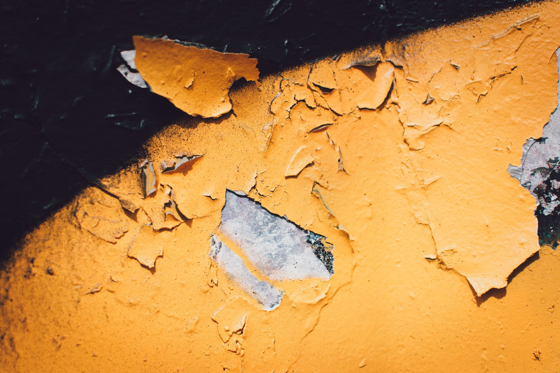 A detailed close-up of peeling yellow paint on a textured wall with visible decay.