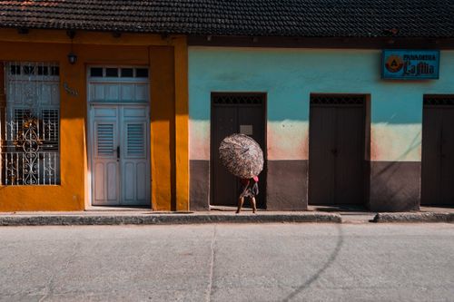 Free Vibrant street view with person holding a floral umbrella walking past colorful buildings. Stock Photo
