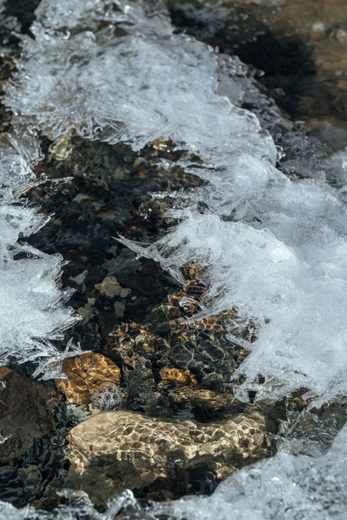 Free A serene winter scene showcasing ice crystals on a creek with visible rocks beneath the water. Stock Photo