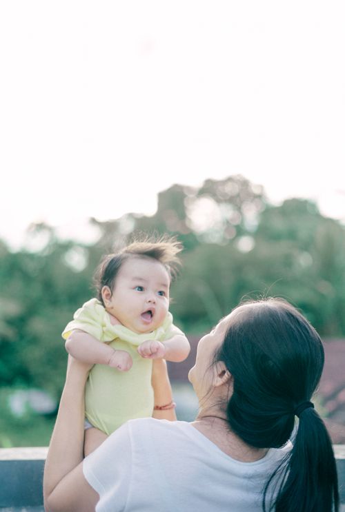 Free A joyful mother lifts her baby under a bright sky, surrounded by a serene outdoor setting. Stock Photo