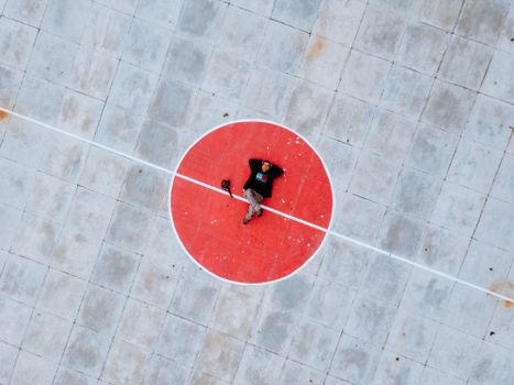 Aerial shot of person lying on a red circle at a concrete sports court. Unique high angle view.