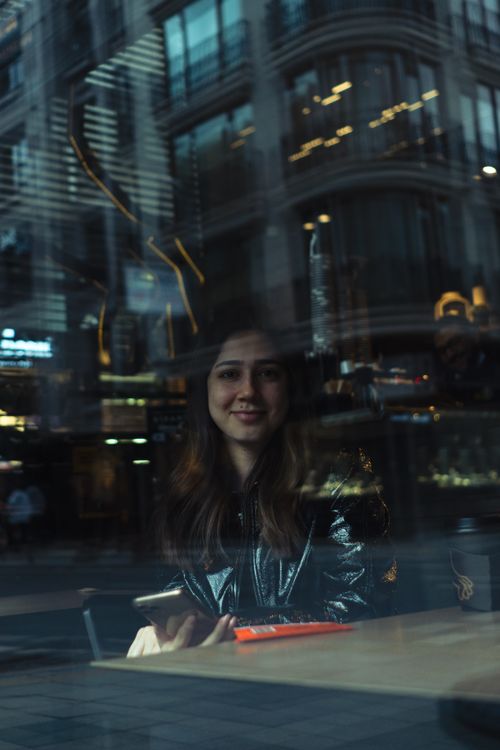 Free A woman smiles through a glass window with city reflections in Istanbul, Turkey. Stock Photo