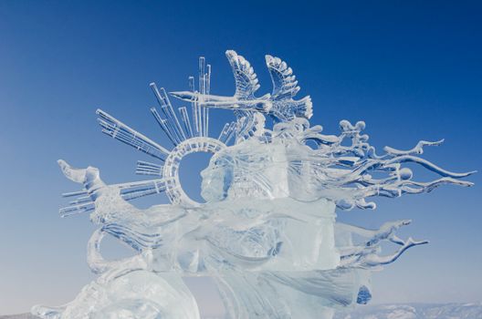A detailed ice sculpture with elaborate designs against a clear blue sky, showcasing artistic craftsmanship.