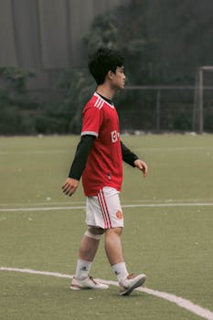 Asian male soccer player wearing a red jersey on a sports field, captured during the day.
