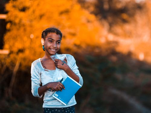 Free A cheerful girl standing outdoors with a notebook against a warm autumn backdrop. Stock Photo
