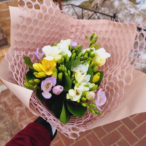 Free A vibrant bouquet of freesias wrapped in pink netting, perfect for any occasion. Stock Photo