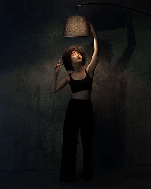 A Woman in Black Tank Top Reaching for the Lamp