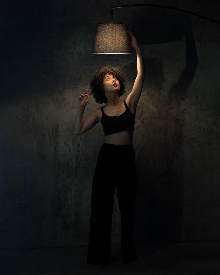 A Woman In Black Tank Top Reaching For The Lamp