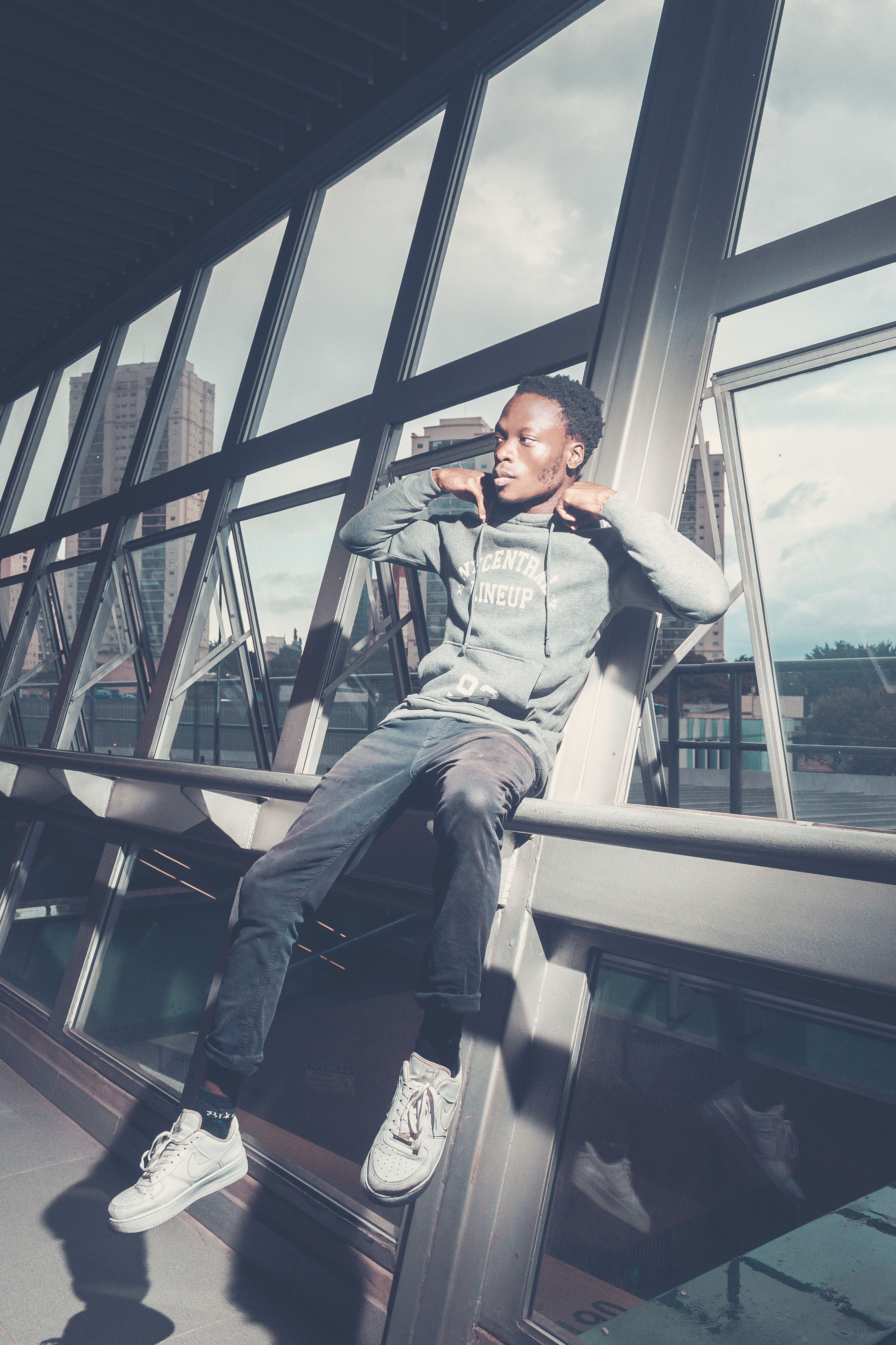Young man in casual hoodie sitting by modern windows indoors.