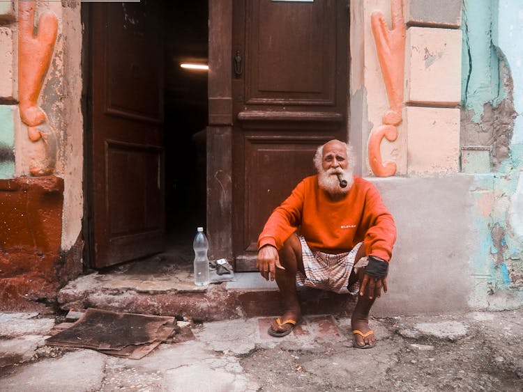 An Elderly Man With A Tobacco Pipe Sitting By A Door