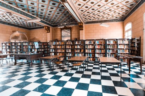 Free Classic library interior featuring checkered flooring, bookshelves, and a detailed ceiling. Stock Photo